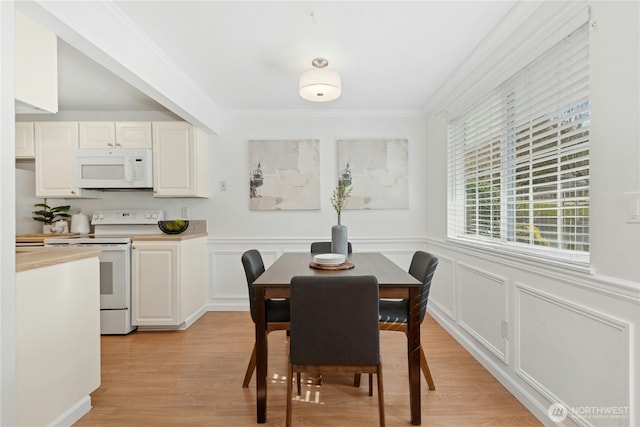 dining area with a decorative wall, wainscoting, light wood finished floors, and ornamental molding