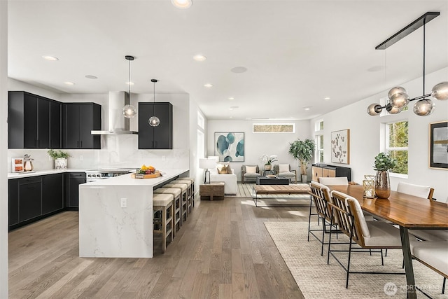 kitchen featuring light wood-type flooring, decorative backsplash, light countertops, wall chimney range hood, and dark cabinets