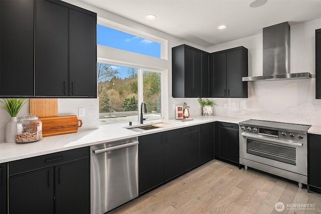 kitchen featuring a sink, stainless steel appliances, wall chimney range hood, and dark cabinets