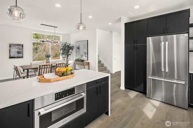 kitchen with light wood finished floors, pendant lighting, recessed lighting, appliances with stainless steel finishes, and dark cabinetry