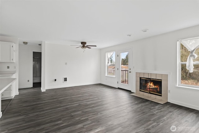 unfurnished living room featuring dark wood finished floors, ceiling fan, baseboards, and a tile fireplace