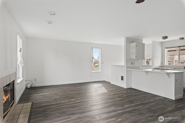 unfurnished living room featuring a tiled fireplace, dark wood-type flooring, baseboards, and a sink