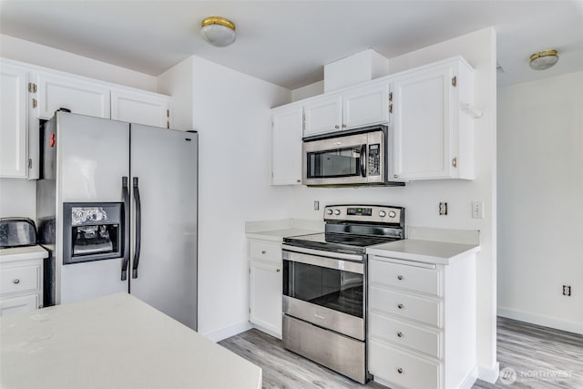 kitchen featuring light wood-type flooring, appliances with stainless steel finishes, white cabinets, light countertops, and baseboards