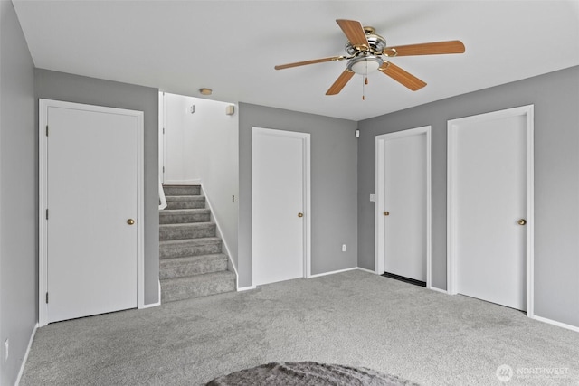 interior space with baseboards, multiple closets, carpet floors, and ceiling fan