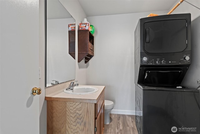 bathroom featuring vanity, wood finished floors, baseboards, stacked washer and clothes dryer, and toilet