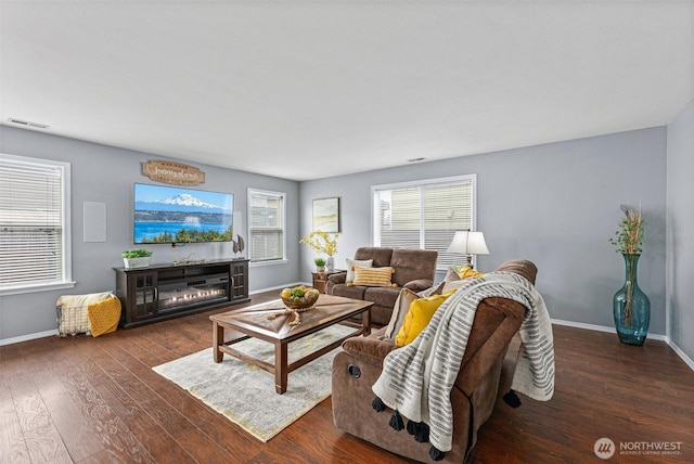 living area featuring a glass covered fireplace, visible vents, baseboards, and wood-type flooring