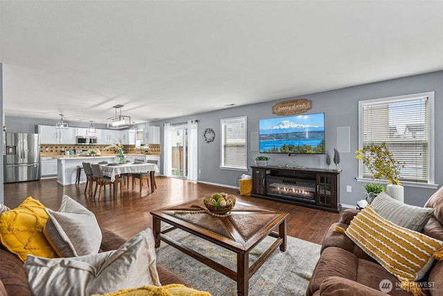 living room with a glass covered fireplace, baseboards, and dark wood finished floors