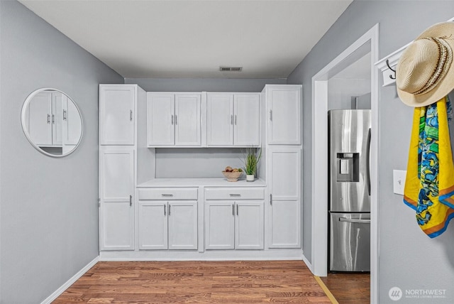 kitchen featuring visible vents, stainless steel fridge with ice dispenser, light countertops, wood finished floors, and white cabinets