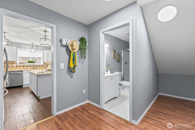 hall featuring a sink, baseboards, lofted ceiling, and wood finished floors