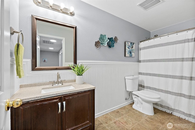 bathroom with a wainscoted wall, toilet, vanity, and visible vents