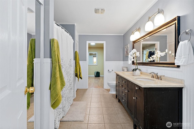 full bathroom with vanity, a wainscoted wall, crown molding, tile patterned floors, and toilet