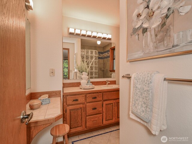 bathroom with tile patterned flooring, a tile shower, and vanity