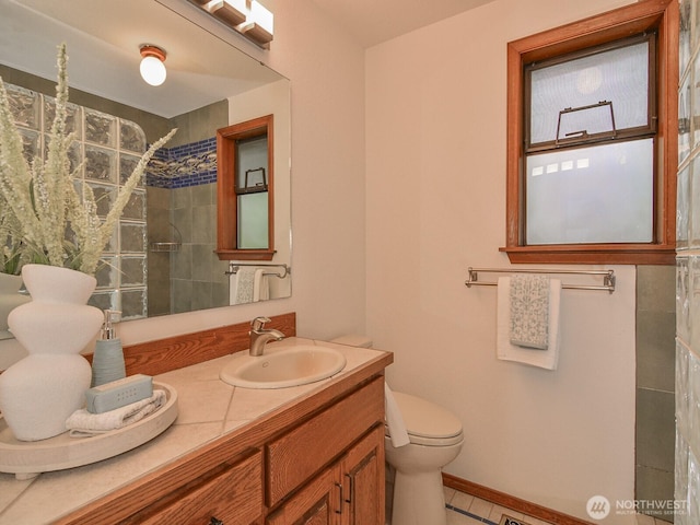 bathroom with baseboards, tiled shower, toilet, and vanity