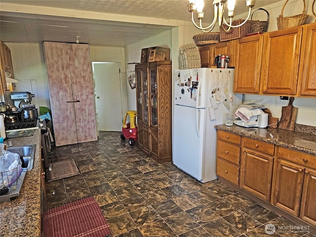 kitchen with dark stone counters, brown cabinets, a notable chandelier, and freestanding refrigerator