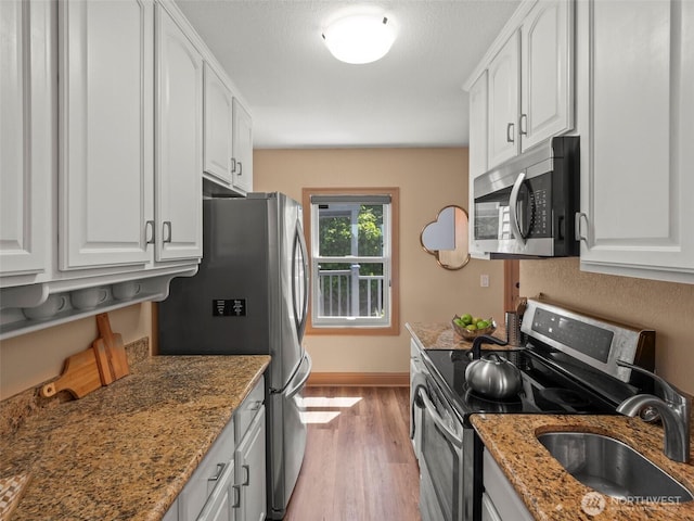 kitchen with light wood finished floors, white cabinetry, stainless steel appliances, and a sink