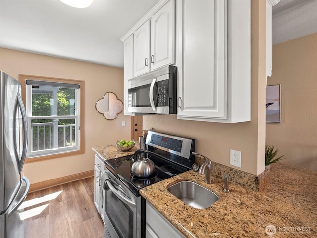 kitchen featuring a sink, stainless steel appliances, light wood-style floors, white cabinets, and light stone countertops