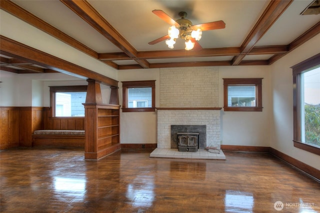 unfurnished living room featuring a wainscoted wall, coffered ceiling, a wood stove, and ceiling fan