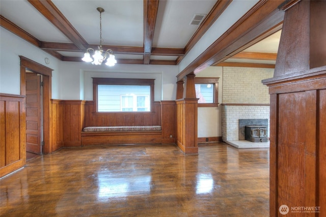 unfurnished living room featuring an inviting chandelier, beam ceiling, wood finished floors, and wainscoting