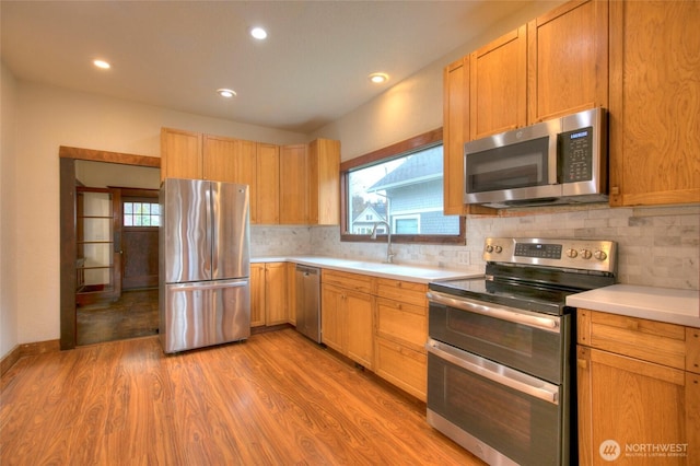 kitchen with backsplash, light wood-style floors, appliances with stainless steel finishes, and light countertops