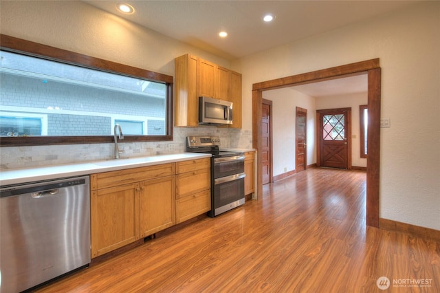 kitchen with tasteful backsplash, light countertops, light wood-style flooring, stainless steel appliances, and a sink