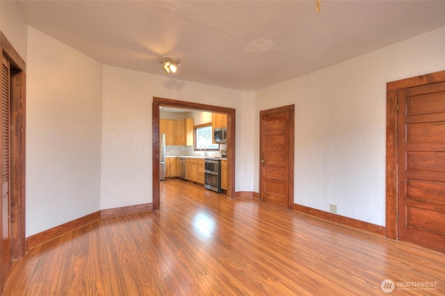 unfurnished living room with wood finished floors, baseboards, and a sink