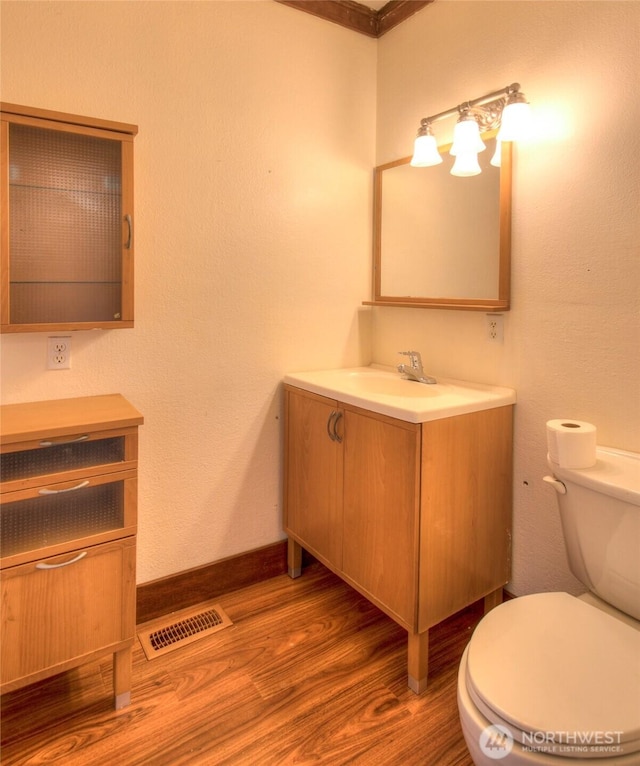 bathroom featuring visible vents, baseboards, toilet, wood finished floors, and vanity