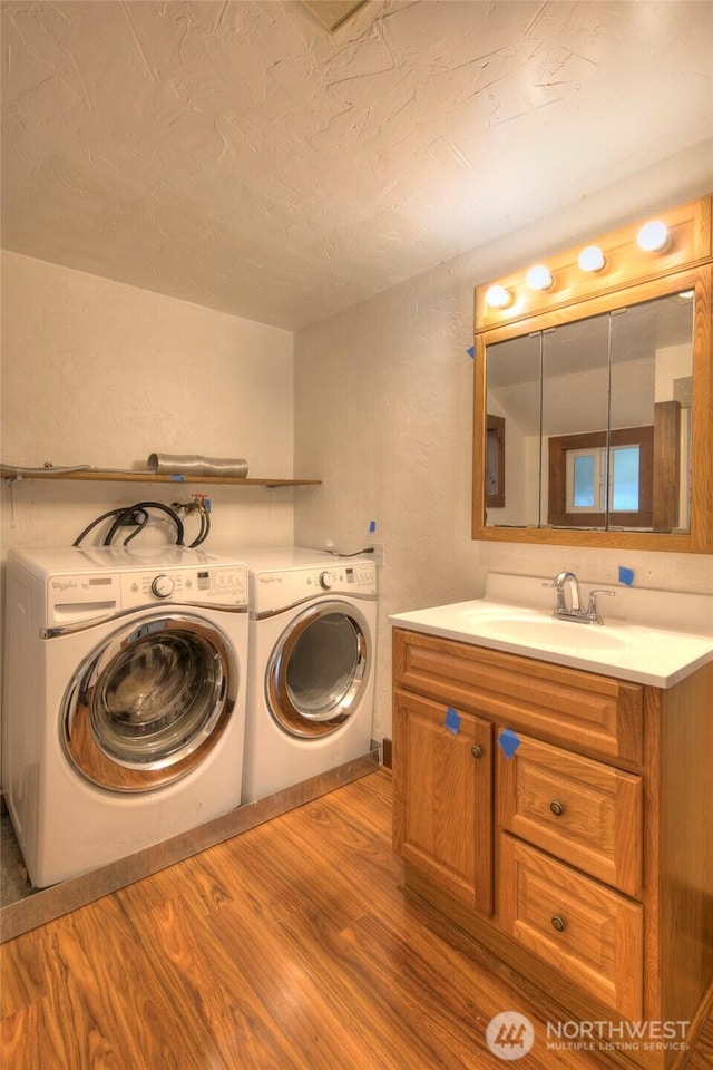 laundry area featuring a textured wall, wood finished floors, washer and dryer, a textured ceiling, and a sink