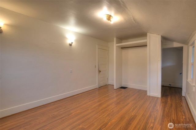 unfurnished bedroom featuring a closet, lofted ceiling, baseboards, and wood finished floors