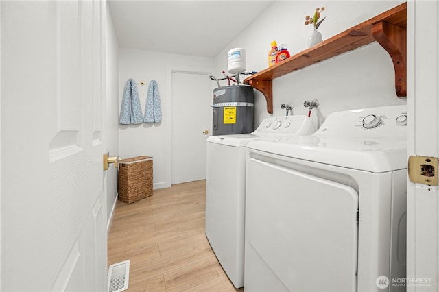 washroom with strapped water heater, laundry area, washer and dryer, and visible vents