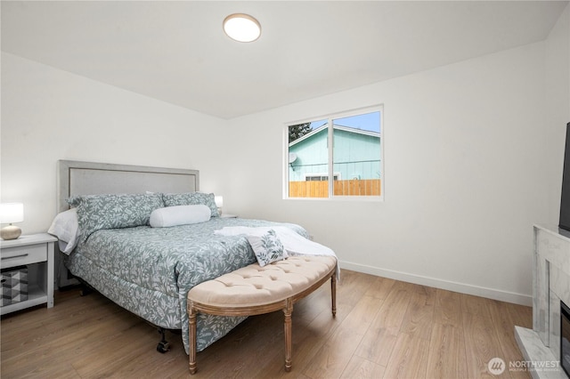 bedroom featuring a fireplace with flush hearth, baseboards, and light wood-style floors