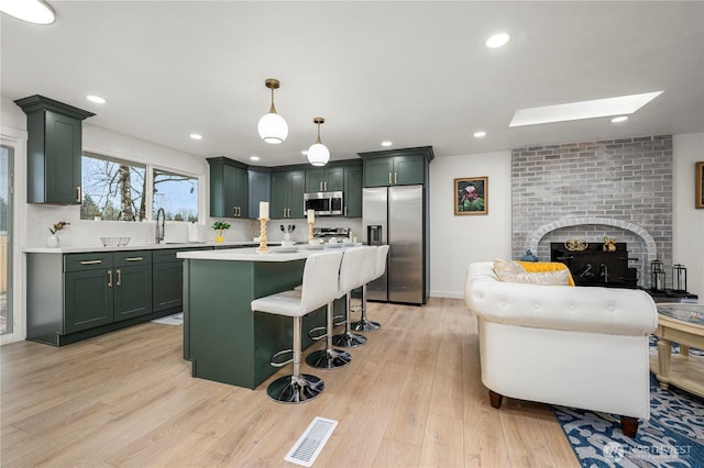 kitchen featuring visible vents, green cabinetry, light countertops, appliances with stainless steel finishes, and a brick fireplace