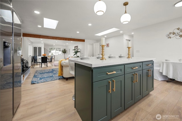 kitchen featuring light wood finished floors, green cabinets, light countertops, a skylight, and stainless steel fridge