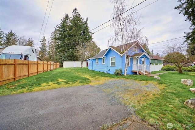 view of front facade with driveway, an outbuilding, a front lawn, and fence