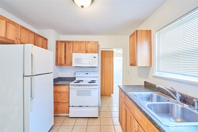 kitchen with dark countertops, light tile patterned floors, brown cabinets, white appliances, and a sink