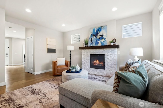 living room featuring a stone fireplace, recessed lighting, wood finished floors, and baseboards