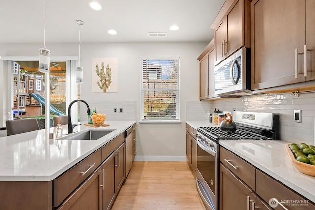 kitchen featuring a sink, light stone counters, appliances with stainless steel finishes, a peninsula, and light wood finished floors