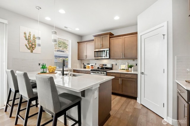 kitchen with visible vents, a sink, decorative backsplash, appliances with stainless steel finishes, and a kitchen bar