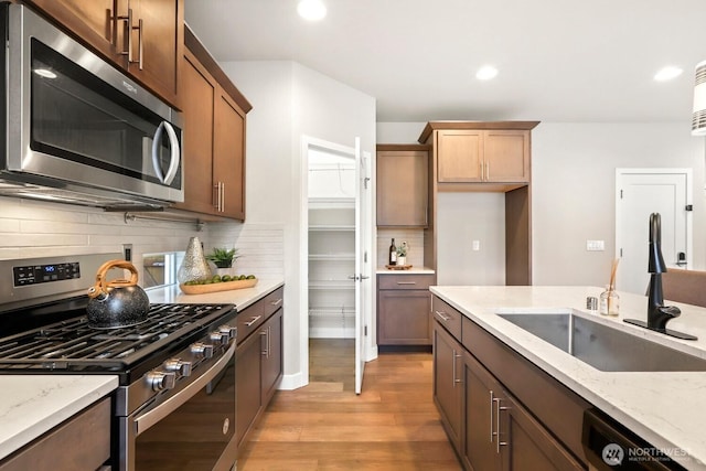 kitchen with light wood-style flooring, a sink, light stone counters, recessed lighting, and stainless steel appliances