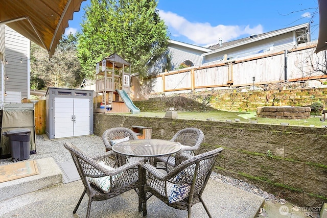 view of patio featuring outdoor dining space, fence, an outdoor structure, a storage shed, and a playground