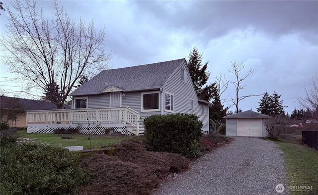 view of front facade featuring a wooden deck, a shingled roof, an outdoor structure, a front lawn, and a detached garage