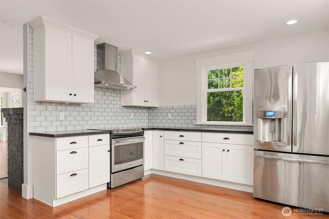 kitchen with dark countertops, decorative backsplash, white cabinets, stainless steel appliances, and wall chimney exhaust hood