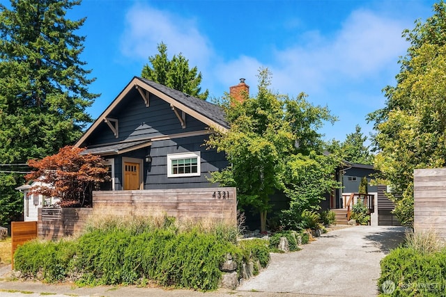 view of front of home featuring driveway, a chimney, and fence