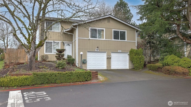 view of front facade featuring aphalt driveway, an attached garage, and fence