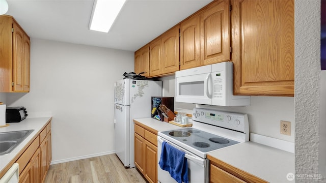 kitchen featuring a sink, white appliances, light wood-style flooring, and light countertops