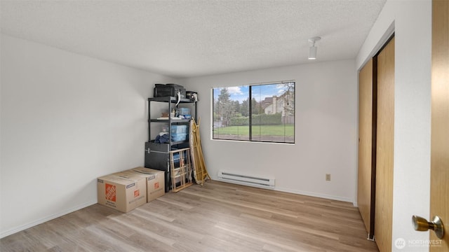 interior space featuring light wood-type flooring, baseboards, baseboard heating, and a textured ceiling