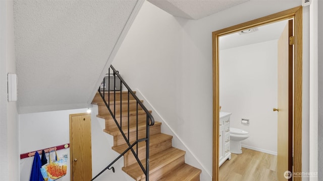 staircase with wood finished floors, baseboards, and a textured ceiling