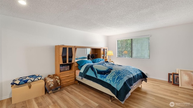 bedroom with baseboards, a textured ceiling, and light wood finished floors