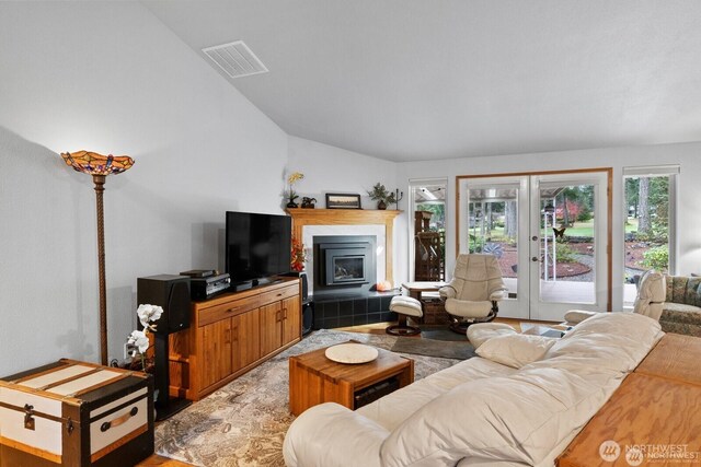 living room with visible vents, lofted ceiling, a fireplace, french doors, and light wood-type flooring