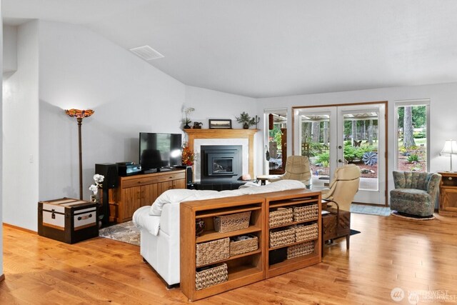 living area with visible vents, lofted ceiling, light wood-style flooring, french doors, and a glass covered fireplace