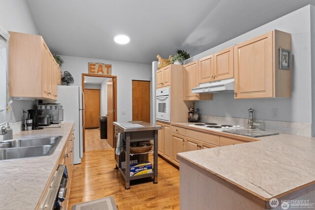 kitchen with white appliances, light brown cabinetry, light countertops, light wood-style floors, and under cabinet range hood